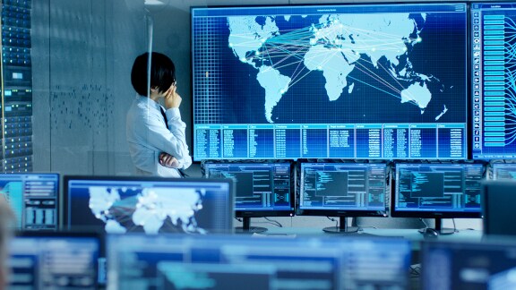 An employee is analyzing the feed from the computers on a big screen