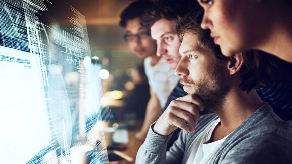 A group of employees looking at the data feeds on the big monitor