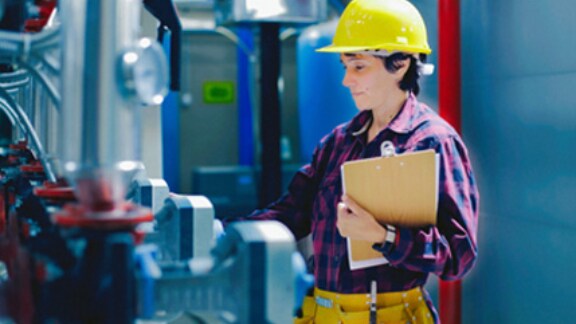 A worker supervising the readings of the machines on the floor of a manufacturing facility